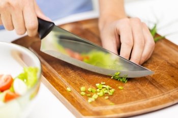 healthy eating, cooking, vegetarian food, dieting and people concept - close up of woman chopping green onion with knife on wooden cutting board