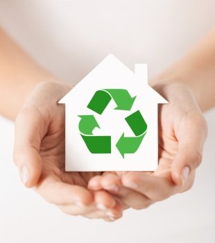 people, ecology, environment and conservation concept - close up of hands holding house with green recycling sign