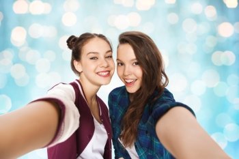 people, friends, teens and friendship concept - happy smiling pretty teenage girls taking selfie over blue holidays lights background
