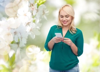 people, technology, communication and leisure concept - happy young woman with smartphone texting message over natural cherry blossom background