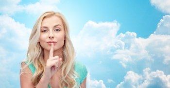 people, gesture and secret concept - beautiful young woman holding finger at her lips over blue sky and clouds background