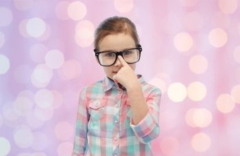 childhood, school, education, vision and people concept - happy little girl in eyeglasses over pink holidays lights background