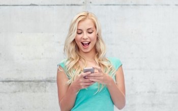 emotions, expressions, technology and people concept - smiling young woman or teenage girl texting on smartphone over gray concrete wall background
