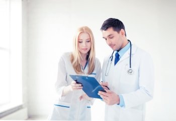 bright picture of two young attractive doctors pointing at blank paper. two young attractive doctors
