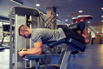 sport, fitness, bodybuilding, lifestyle and people concept - man exercising and flexing muscles on leg curl machine in gym
