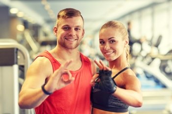sport, fitness, lifestyle, gesture and people concept - smiling man and woman showing ok hand sign in gym