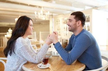 people, love, romance and dating concept - happy couple drinking tea and holding hands at cafe or restaurant