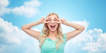 emotions, expressions, positive gesture and people concept - smiling young woman or teenage girl showing peace hand sign with both hands over blue sky and clouds background