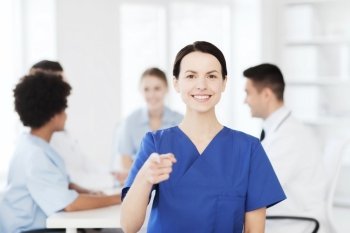 clinic, profession, people and medicine concept - happy female doctor or nurse over group of medics meeting at hospital pointing finger to you