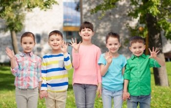 childhood, fashion, friendship and people concept - group of happy smiling little children holding hands over summer campus background