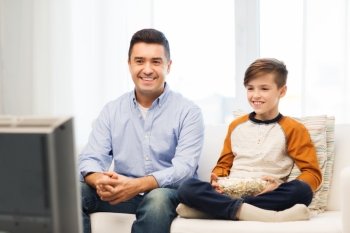 family, people, technology, television and entertainment concept - happy father and son with popcorn watching tv at home