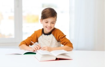 education, childhood, people, homework and school concept - smiling student boy with book writing to notebook at home