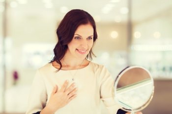 sale, consumerism, shopping and people concept - happy woman choosing and trying on pendant at jewelry store