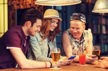 people, leisure, friendship and communication concept - group of happy smiling friends with smartphones and drinks at bar or pub