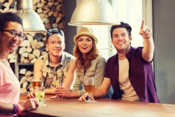 people, leisure, friendship and communication concept - group of happy smiling friends drinking beer and cocktails at bar or pub and pointing finger to something