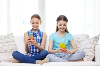 people, children, technology, friends and friendship concept - happy little girls with smartphones sitting on sofa at home