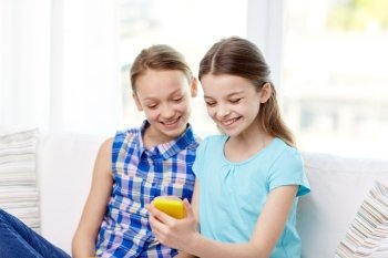 people, children, technology, friends and friendship concept - happy little girls with smartphone sitting on sofa at home