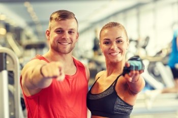 sport, fitness, lifestyle, gesture and people concept - happy man and woman pointing finger to you in gym