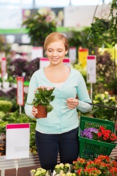 people, gardening, shopping, sale and consumerism concept - happy woman with basket choosing and buying flowers in greenhouse