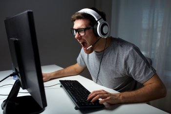 technology, gaming, entertainment, let&#39;s play and people concept - angry screaming young man in headset with pc computer playing game at home and streaming playthrough or walkthrough video