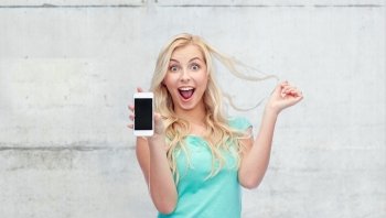 emotions, expressions, technology and people concept - smiling young woman or teenage girl showing blank smartphone screen over gray concrete wall background