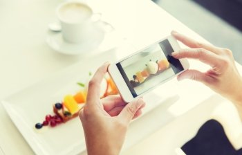 people, holidays, technology, food and lifestyle concept - close up of woman with smartphone taking picture of dessert at restaurant