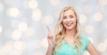 positive gesture and people concept - smiling young woman or teenage girl showing peace hand sign over holidays lights background. smiling young woman or teenage girl showing peace