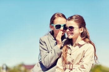 people, children and friendship concept - happy little girl in sunglasses whispering her secret to friends ear or gossiping outdoors