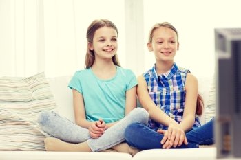 people, children, television, friends and friendship concept - two happy little girls watching tv at home