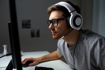 technology, gaming, entertainment, let&#39;s play and people concept - young man in headset and glasses with pc computer playing game at home and streaming playthrough or walkthrough video