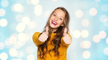 people, gesture, style and fashion concept - happy young woman or teen girl in casual clothes showing thumbs up over blue holidays lights background