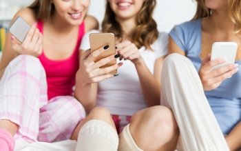 friendship, people, pajama party and technology concept - close up of happy friends or teenage girls with smartphones at home