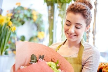 people, business, sale and floristry concept - happy smiling florist woman holding bunch of flowers wrapped into paper at flower shop
