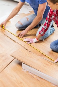 repair, building, flooring and people concept - close up of happy couple with ruler measuring parquet board at home