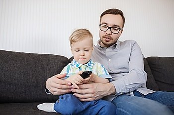 family, childhood, fatherhood, technology and people concept - happy father helping little son with remote control and watching tv at home
