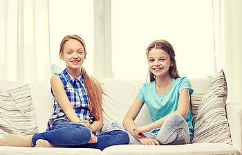 people, children, friends and friendship concept - happy little girls sitting on sofa at home