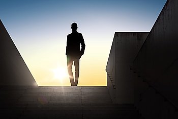 business and people concept - silhouette of businessman standing on stairs over sun light background. silhouette of businessman over sun light