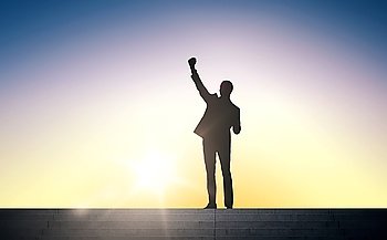 business, success, gesture and people concept - silhouette of happy businessman raising fist and celebrating victory standing on stairs over sun light background