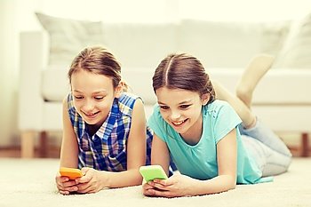 people, children, technology, friends and friendship concept - happy little girls with smartphones lying on floor at home