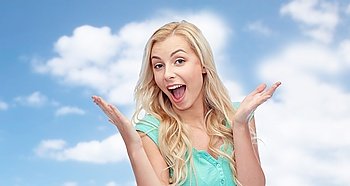 emotions, expressions and people concept - surprised smiling young woman or teenage girl over blue sky and clouds background