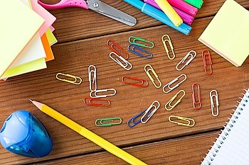 education, school supplies, stationery and object concept - close up of clips, pens and stickers on wooden table