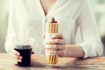 fast food, people and unhealthy eating concept - close up of woman hands with hot dog and cola drink sitting at table