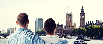 people, homosexuality, same-sex marriage, travel and love concept - close up of happy male gay couple hugging from back over big ben and houses of parliament in london background