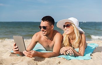 love, travel, tourism, technology and people concept - happy couple on vacation with tablet pc computer sunbathing on summer beach
