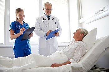 medicine, age, health care and people concept - doctor and nurse with clipboards visiting senior patient woman at hospital ward