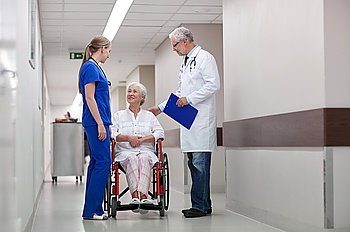 medicine, age, health care and people concept - doctor, nurse and senior woman patient in wheelchair at hospital corridor