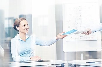 business and people concept - smiling businesswoman receiving papers from someone in office. businesswoman taking papers from someone in office
