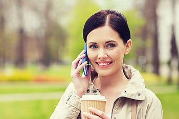 drinks, leisure, technology and people concept - smiling woman with coffee calling and talking on smartphone in park