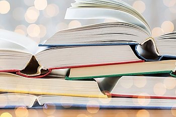 education, school, literature, reading and knowledge concept - close up of books on wooden table over holidays lights background