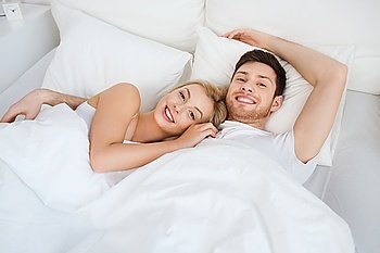 people, rest, love, relationships and happiness concept - happy smiling couple lying in bed at home